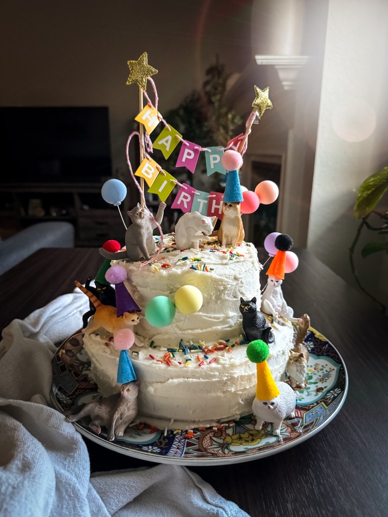 Four layer chocolate birthday cake with white vanilla buttercream frosting, cat decorations, and a Happy Birthday banner